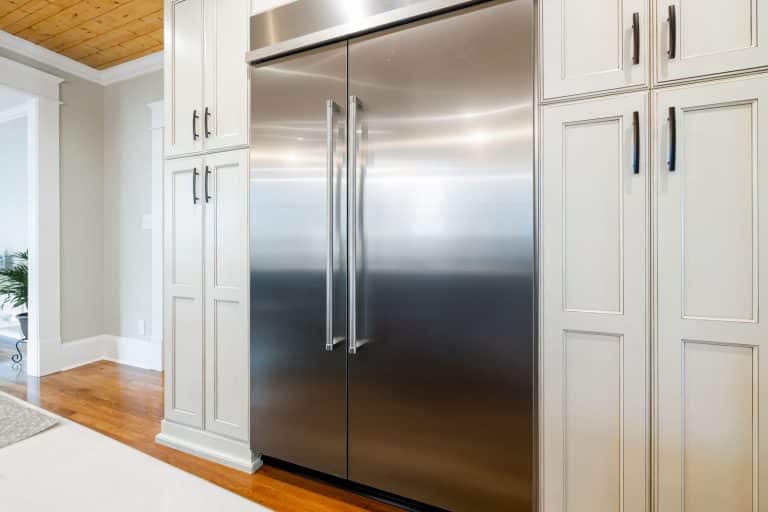 Built-in stainless steel household refrigerator between white kitchen cabinets